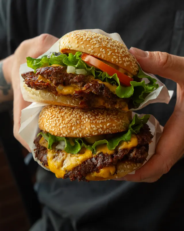 Two cheeseburgers stacked in a pair of hands